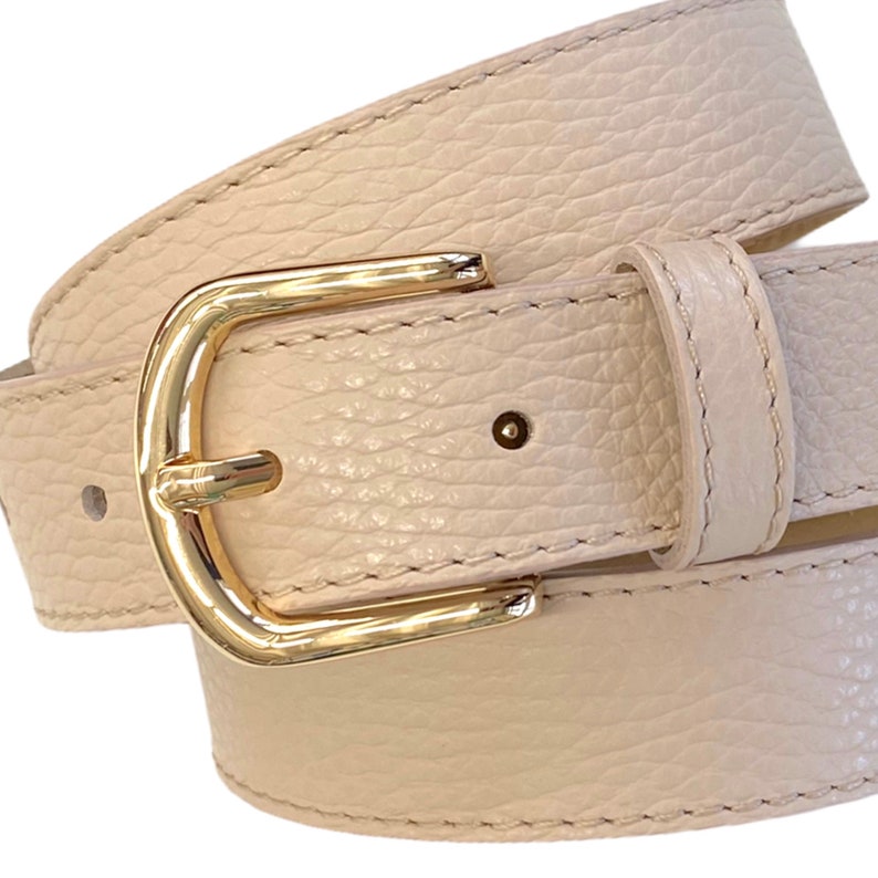 May include: A light beige leather belt with a gold buckle. The belt is folded in half and the buckle is in the center of the image.