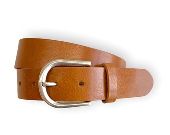Peut inclure: Une ceinture en cuir beige avec une surface lisse et texturée, dotée d'une boucle en métal argenté arrondie. La ceinture comprend un passant en cuir assorti et plusieurs trous pré-percés le long de la sangle pour le réglage.