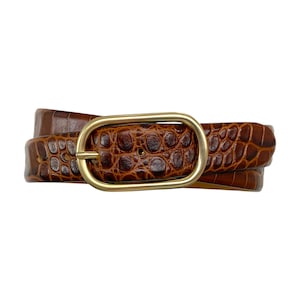 May include: A brown belt with a textured crocodile-embossed pattern and a smooth, oval-shaped gold-tone metal buckle. The belt strap features a consistent reptilian scale design throughout, secured by a polished, rounded metallic buckle frame.