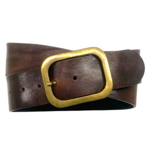 May include: A dark brown leather belt featuring a smooth, weathered texture and a rectangular brass buckle with a rounded frame. The belt strap includes visible pre-punched holes for adjustment and exhibits a natural, worn-in appearance.