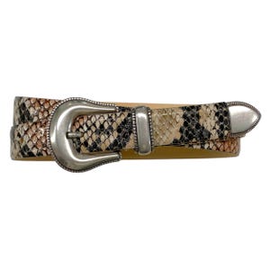 May include: A snakeskin-patterned belt with a silver-colored buckle and tip. The belt features a mix of brown, black, and beige tones, creating a textured appearance. The buckle is a large, curved design, adding a touch of Western flair.