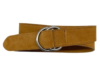 May include: A tan suede belt featuring a double silver-toned metal ring buckle. The belt has a textured, matte finish and is constructed with visible stitching along the edges of the strap, securing the circular hardware in place.