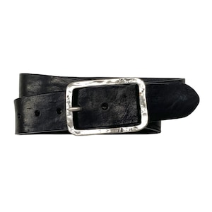 Peut inclure: Une ceinture noire à la surface sombre et texturée, dotée d'une grande boucle rectangulaire argentée. La boucle présente une finition martelée et irrégulière avec des coins arrondis et un ardillon central, fixée par des coutures visibles.
