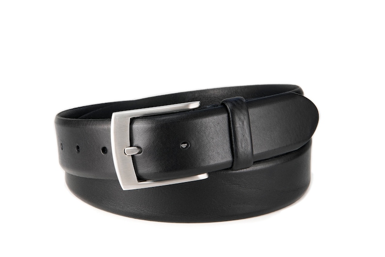 May include: A black leather belt featuring a smooth finish and a rectangular silver-toned metal buckle. The belt includes a matching leather keeper loop and a series of punched holes for adjustment, presented in a coiled, circular configuration.