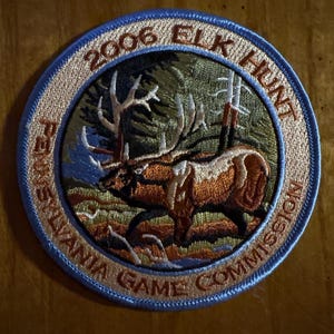 May include: Embroidered patch with a circular design featuring a brown elk with large antlers in a forest setting. The patch has a blue border with the text "2006 ELK HUNT" and "PENNSYLVANIA GAME COMMISSION".