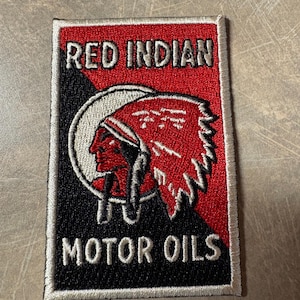May include: Embroidered patch with the words "RED INDIAN MOTOR OILS" in white lettering. The patch features a Native American profile in a red headdress, set against a red and black background, with a white border.