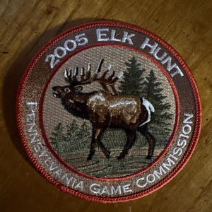 May include: Embroidered patch with a brown elk in a forest scene. The patch is circular with the text "2005 ELK HUNT" and "PENNSYLVANIA GAME COMMISSION" in a circular pattern around the elk.