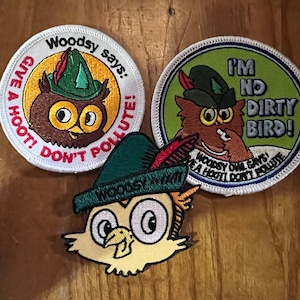 May include: Three embroidered patches featuring an owl character wearing a green hat. One patch says "Give a hoot! Don't pollute!" Another says "I'm no dirty bird!" The third patch is the owl's face.