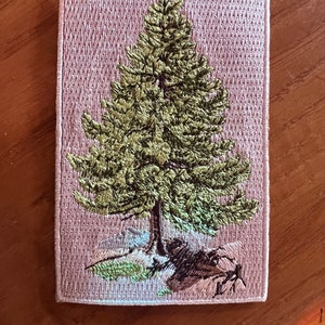 May include: Embroidered patch featuring a green pine tree on a pink background. The tree is detailed with brown branches and a light brown trunk. The patch is surrounded by a white border.