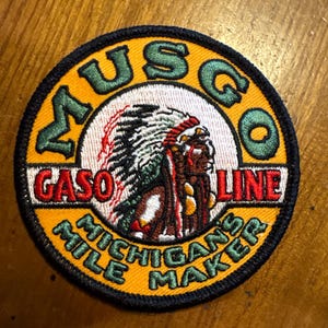 May include: Round patch with the text "MUSCO GASOLINE" in green and red, and "MICHIGAN'S MILE MAKER" in green. The patch features an illustration of a Native American chief in a headdress.