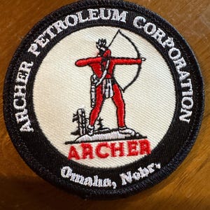May include: Round patch with a black border and the words "ARCHER PETROLEUM CORPORATION" in white. The center features a red archer with a bow and arrow. Below the archer is the word "ARCHER" in red, and "Omaha, Nebr." in white.