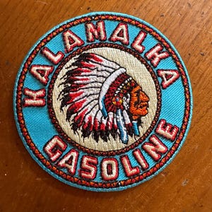 May include: Round patch with a turquoise border and the words "KALAMALKA GASOLINE" in orange lettering. The center features an illustration of a Native American chief in a headdress with red, black, and white feathers.