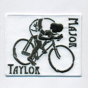 May include: A white embroidered patch with a black silhouette of a cyclist riding a bicycle. The text "MAJOR TAYLOR" is embroidered in black on the patch.
