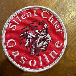 May include: Round, red patch with the words "Silent Chief Gasoline" embroidered in white. The patch features an image of a Native American chief in brown and white, with a white border.