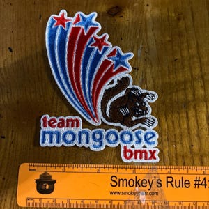 May include: A white embroidered patch with a brown cartoon squirrel, red and blue stars, and the text "team mongoose bmx".