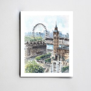 May include: Watercolor print of London landmarks, including the London Eye, Big Ben, and Westminster Abbey. The artwork features a high-angle view with soft blues, greens, and browns, capturing the city's architecture and the Thames River.
