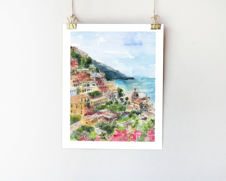 May include: Watercolor painting of a colorful Italian village on a hillside overlooking the ocean. The village is painted in shades of yellow, orange, red, and brown. The ocean is a light blue color and the sky is a pale blue with white clouds. There are green trees and bushes in the foreground.