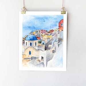 May include: Watercolor painting of a blue-domed church in a whitewashed village, with a view of the surrounding buildings and a blue sky.
