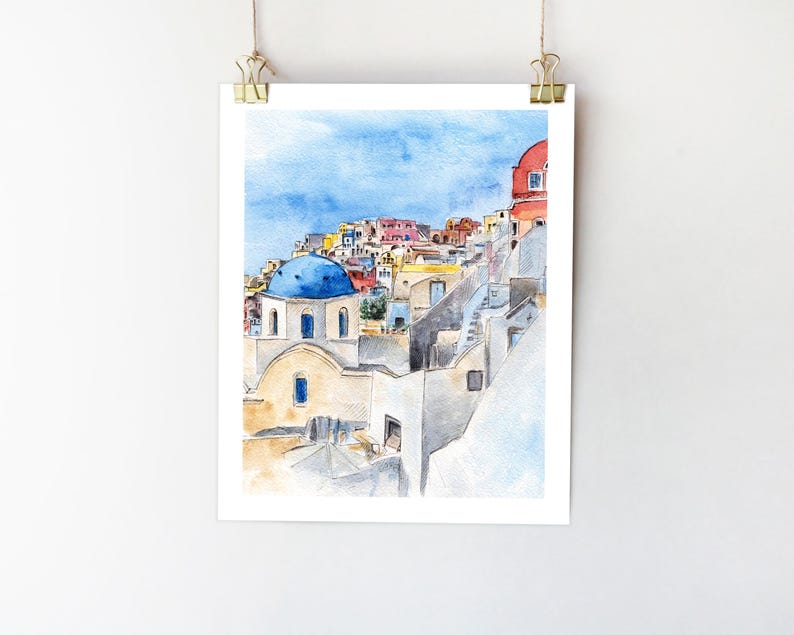 May include: Watercolor painting of a blue-domed church in a whitewashed village, with a view of the surrounding buildings and a blue sky.
