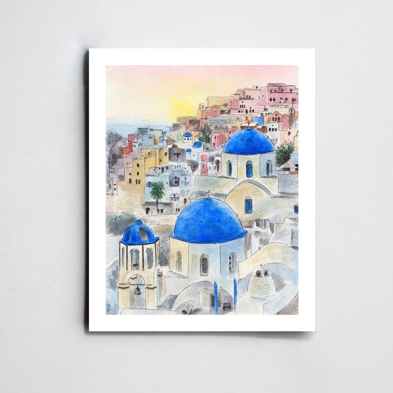May include: Watercolor painting of a white building with blue domed roofs in a village setting. The buildings are clustered together and have a rustic, Mediterranean feel. The sky is a soft pink and orange, suggesting a sunset or sunrise.