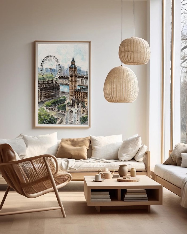 May include: A watercolor print of London's skyline, including the London Eye and Big Ben, in a wooden frame. The artwork hangs above a light-colored sofa with neutral-toned throw pillows. Two woven pendant lights hang from the ceiling.