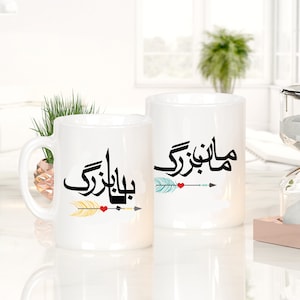 May include: Two white ceramic mugs with black Arabic calligraphy and colorful arrow designs. The mugs are on a white surface with a glass hourglass on a wooden base.