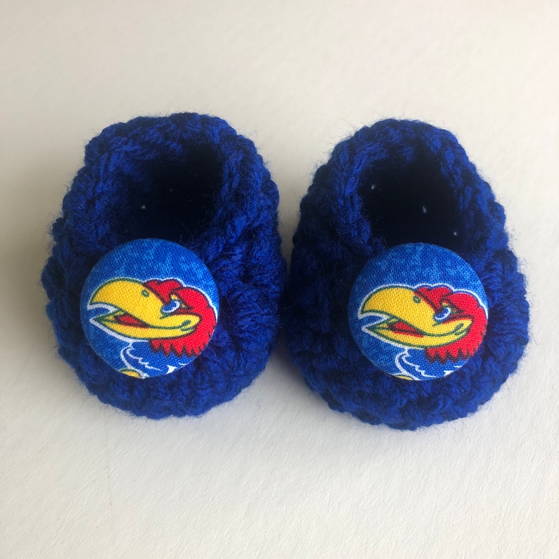 May include: A pair of blue crocheted baby booties with a blue, yellow, and red button featuring a bird mascot.