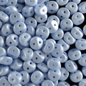 Pu&ograve; includere: Un mucchio di perline di vetro blu chiaro con due fori in ogni perlina. Le perline sono lisce e hanno una finitura leggermente iridescente.