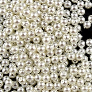 May include: A large pile of white pearl beads. The beads are round and smooth, and they are all the same size.