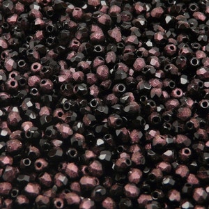 May include: A close-up image of a large quantity of small, faceted, dark purple glass beads. The beads have a glittery, iridescent finish.