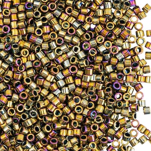 May include: A close-up shot of a pile of small, cylindrical beads. The beads have a metallic finish with gold, silver, and iridescent purple hues. They are scattered across a white background, suggesting they are for crafting or jewelry making.