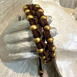 May include: A brown leather bracelet with gold beads woven into the design. The bracelet has a simple tie closure.