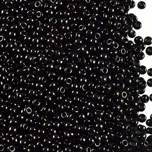 May include: A large quantity of small, black, round seed beads. The beads are arranged in a pile, with some spilling out over the edge.