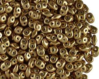 Può includere: Primo piano di un mucchio di perline di vetro ceche color oro. Ogni perlina ha due fori e una forma arrotondata. Le perline sono sparse, creando una superficie strutturata.