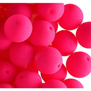 May include: A close-up of numerous bright pink, spherical beads. Each bead has a small hole, indicating they are designed for threading. The beads have a matte finish and are densely packed together. These are likely craft supplies, possibly for jewellery making.