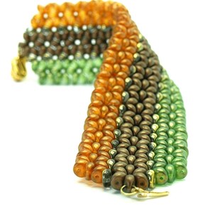 May include: A multi-coloured beaded bracelet with orange, brown and green beads. The bracelet is made with small, round beads and has a gold clasp.