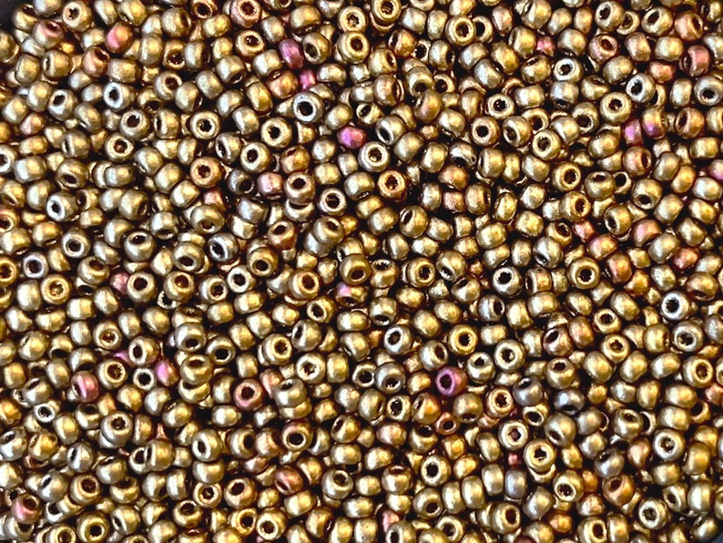 Puede incluir: Una imagen de primer plano de una gran cantidad de peque&ntilde;as cuentas redondas de color dorado. Las cuentas tienen un brillo met&aacute;lico y una ligera calidad iridiscente.