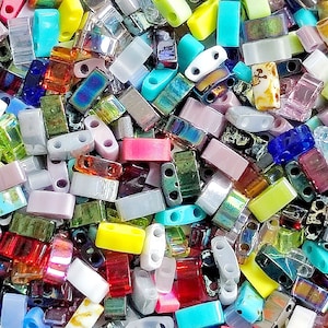 May include: A large assortment of colorful glass beads in various shapes and sizes. The beads are mostly rectangular and have two holes on each side. The beads are a mix of opaque and translucent colors, including blue, green, red, yellow, purple, and white.