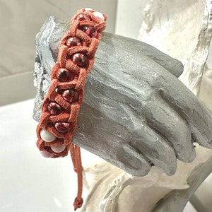 May include: A braided leather bracelet with red and white beads. The bracelet is tied with a knot and has a tassel.