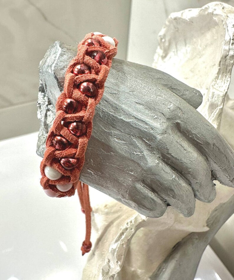 May include: A braided leather bracelet with red and white beads. The bracelet is tied with a knot and has a tassel.