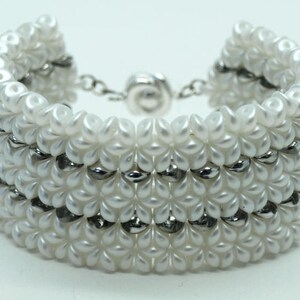 May include: White beaded bracelet with silver accents. The bracelet is made of small, round beads and has a magnetic clasp.
