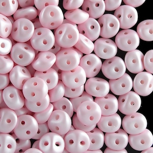 May include: A large group of pink, two-holed beads. The beads are smooth and have a pearlescent finish.