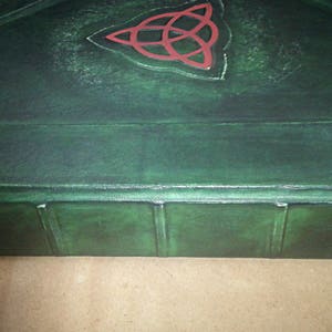 May include: A dark green leather-bound book with a red Celtic knot design on the cover. The book has a raised spine with five sections.
