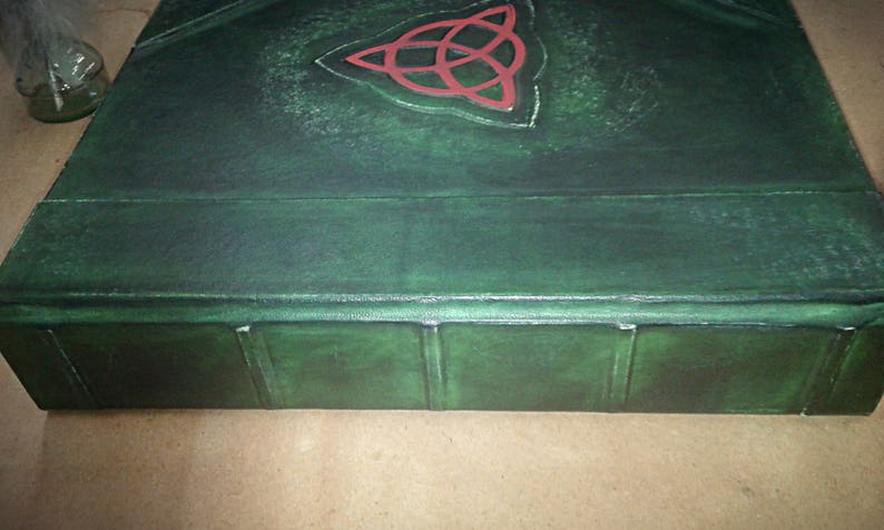 May include: A dark green leather-bound book with a red Celtic knot design on the cover. The book has a raised spine with five sections.