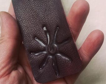 May include: A dark brown leather bookmark with a star-shaped design embossed on the front.