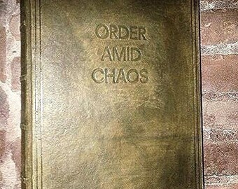 May include: A rectangular book with a distressed olive green cover featuring the embossed text ORDER AMID CHAOS on the front. The book has a double-lined border and three thin ribbon bookmarks in navy blue, light gray, and white extending from the bottom.