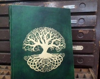 May include: A green leather-bound journal with a gold tree of life design on the front cover. The journal is sitting on a wooden surface.