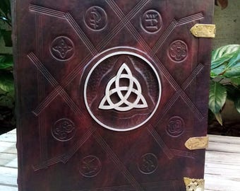 May include: A dark brown leather-bound journal with a silver Celtic knot design on the front cover. The journal has decorative brass corners and clasps.