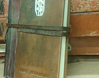 May include: A brown leather-bound journal with a white embossed symbol and the text "NEWT SCAMANDER" on the cover.