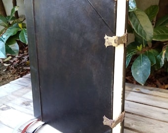 May include: A black leather-bound journal with brass clasps and corner accents. The journal has a white spine and is closed.